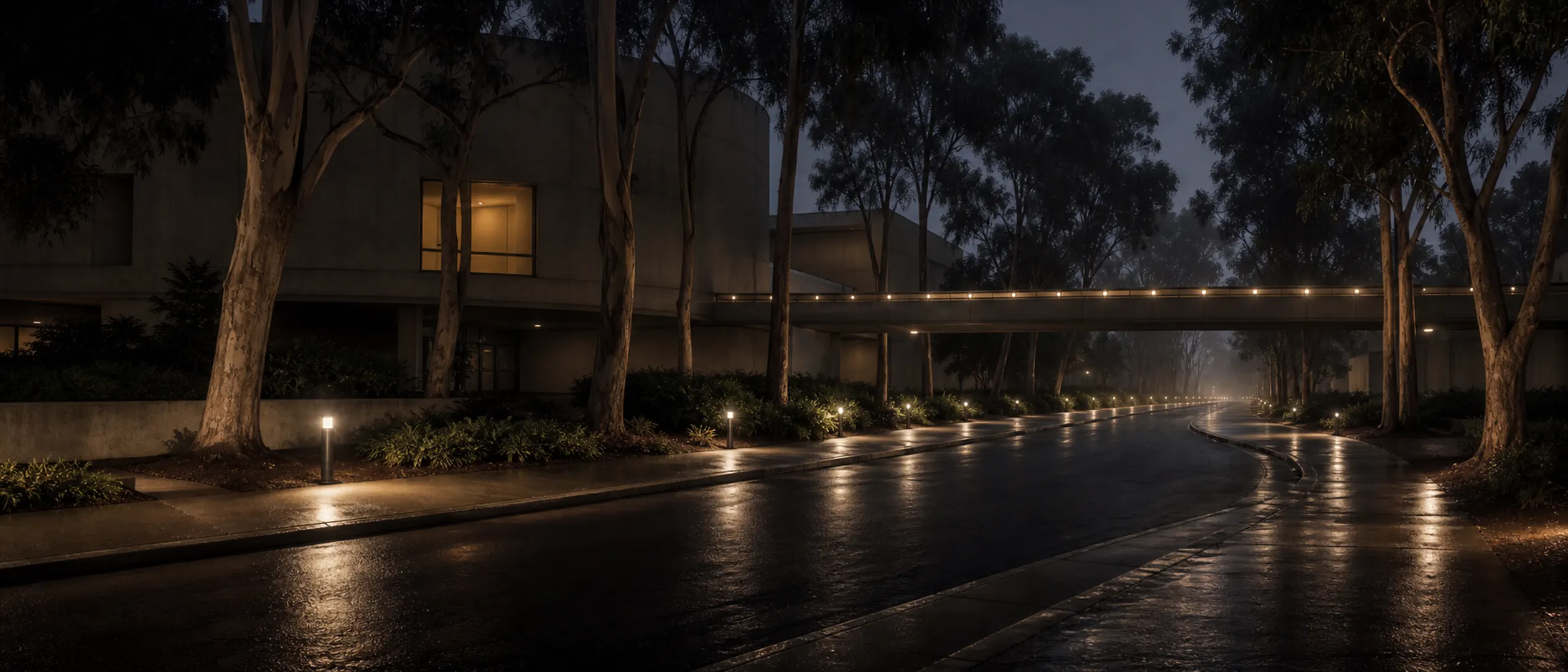 A curving UCI campus road passes eucalyptus trees, concrete buildings, and a pedestrian bridge at blue hour.