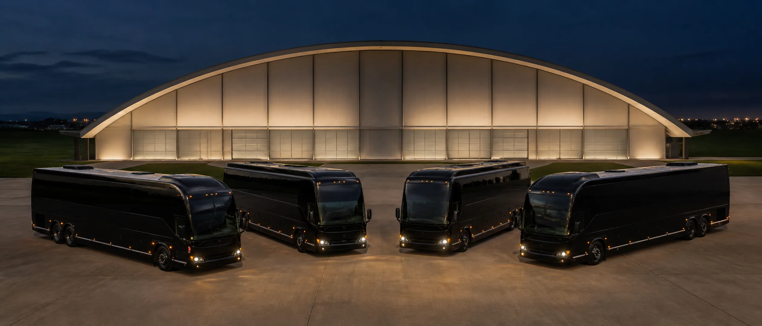 Four near-black motorcoaches form a parked arc before Hangar 244 at Orange County Great Park.