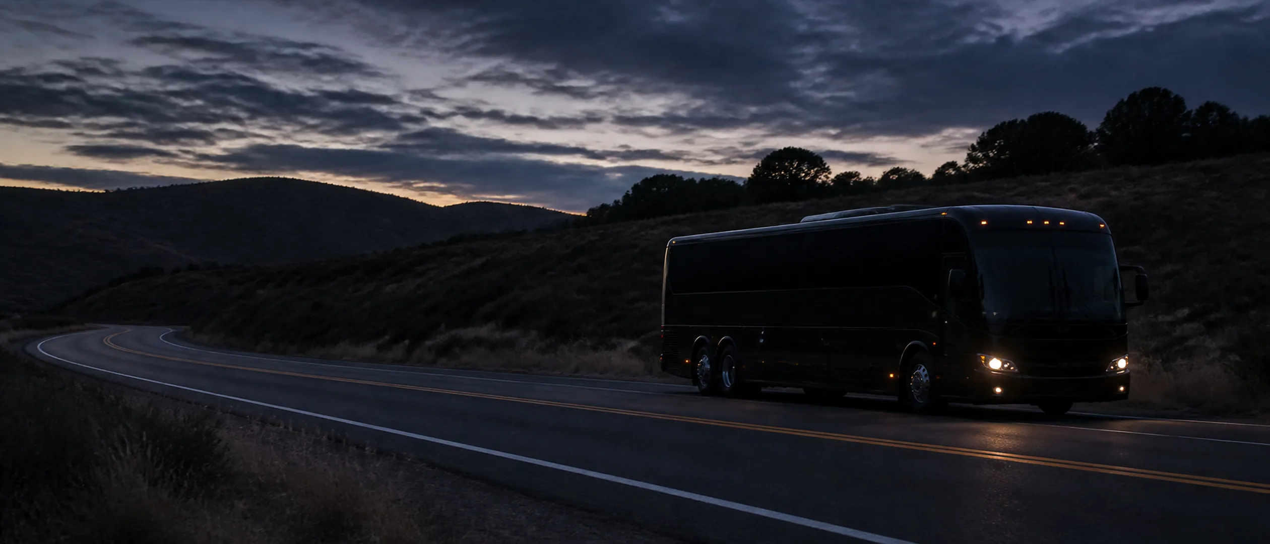 A near-black motorcoach follows a curving road through Irvine Open Space beneath the San Joaquin Hills.
